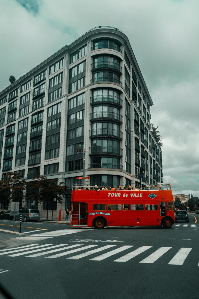 Red Double-Decker Tour Bus Driving past a Modern Building in Montreal, Canada